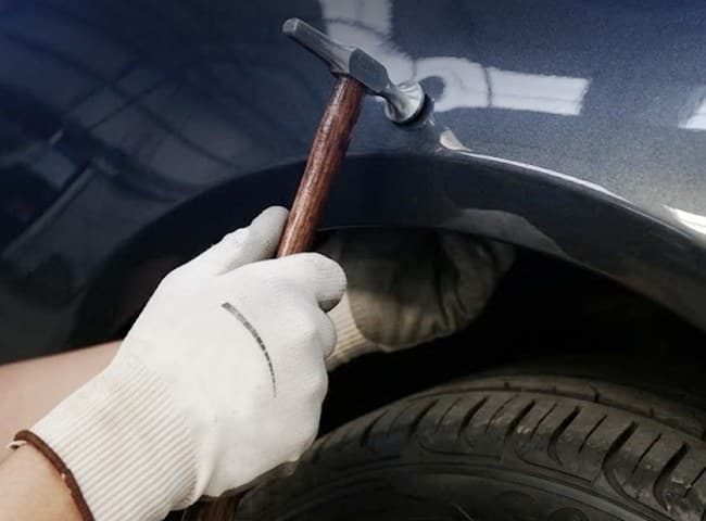 Mão de luva com o martelinho junto à lataria e à roda de um carro