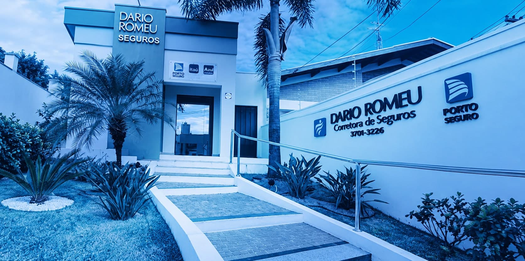 Fachada da Dario Romeu Corretora de Seguros: o pilar com o letreiro Dario Romeu Seguros e o muro com o logo e o telefone 3701-3226