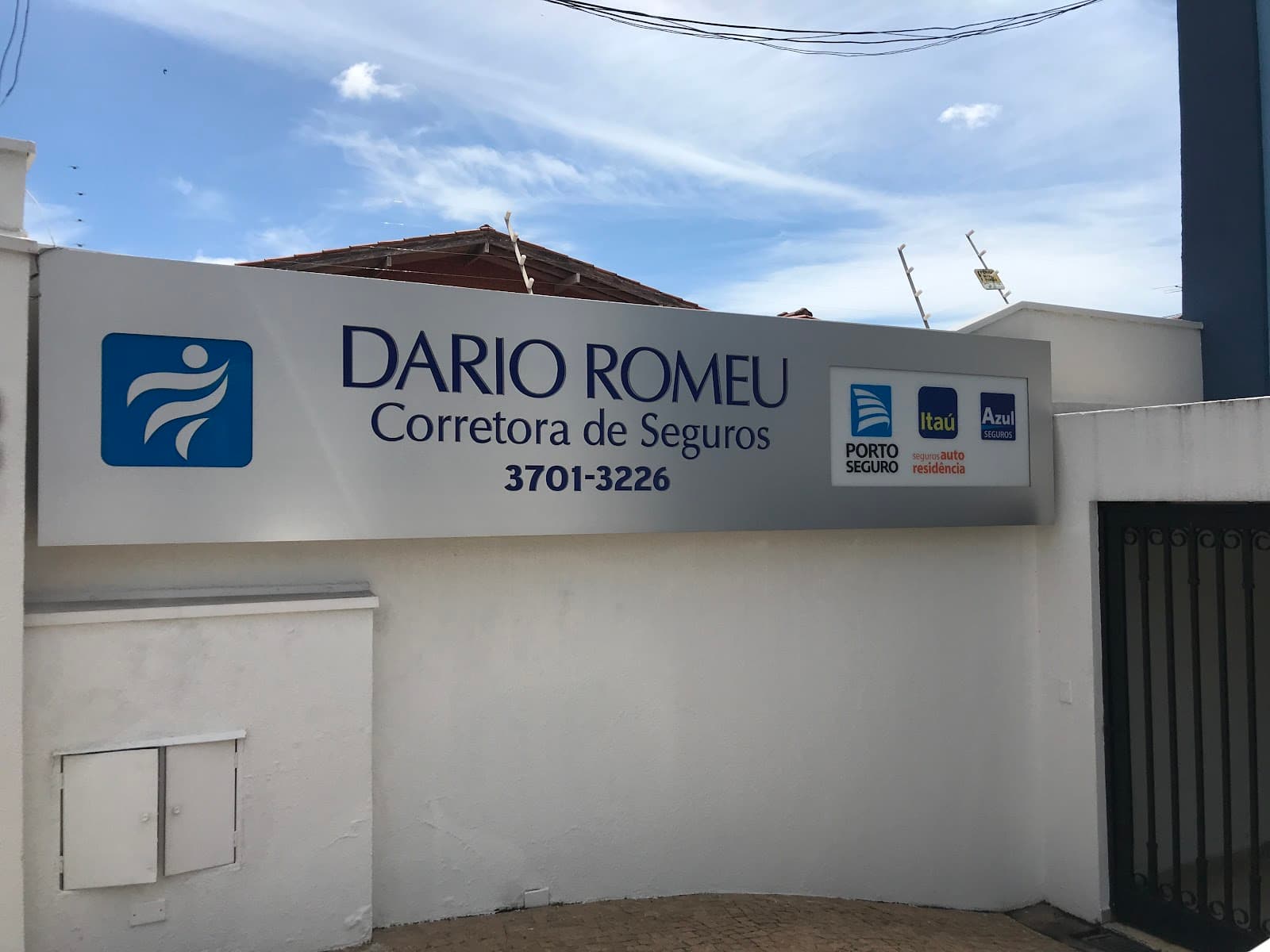 Placa da Dario Romeu Corretora de Seguros no muro, com o telefone 3701-3226 e os selos da Porto Seguro, Itaú e Azul Seguros