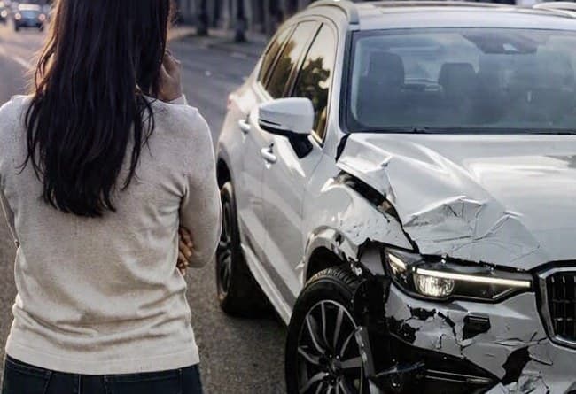 Mulher ao telefone ao lado de um carro branco com a frente batida