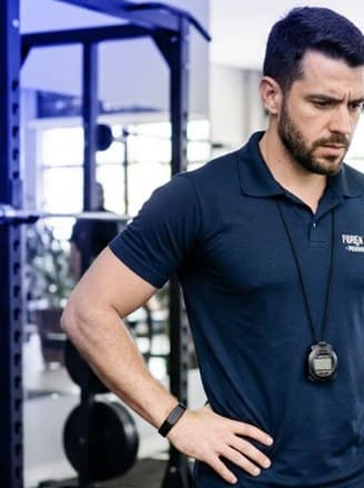Personal trainer de braços na cintura acompanhando um treino na academia